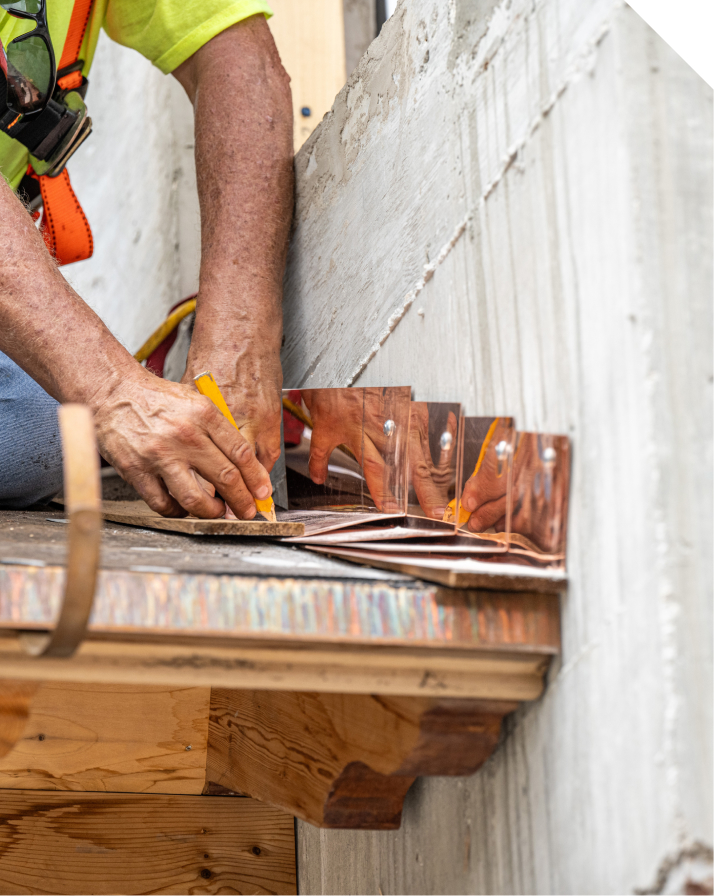 Craftsman hand-marking copper flashing pieces on a parapet