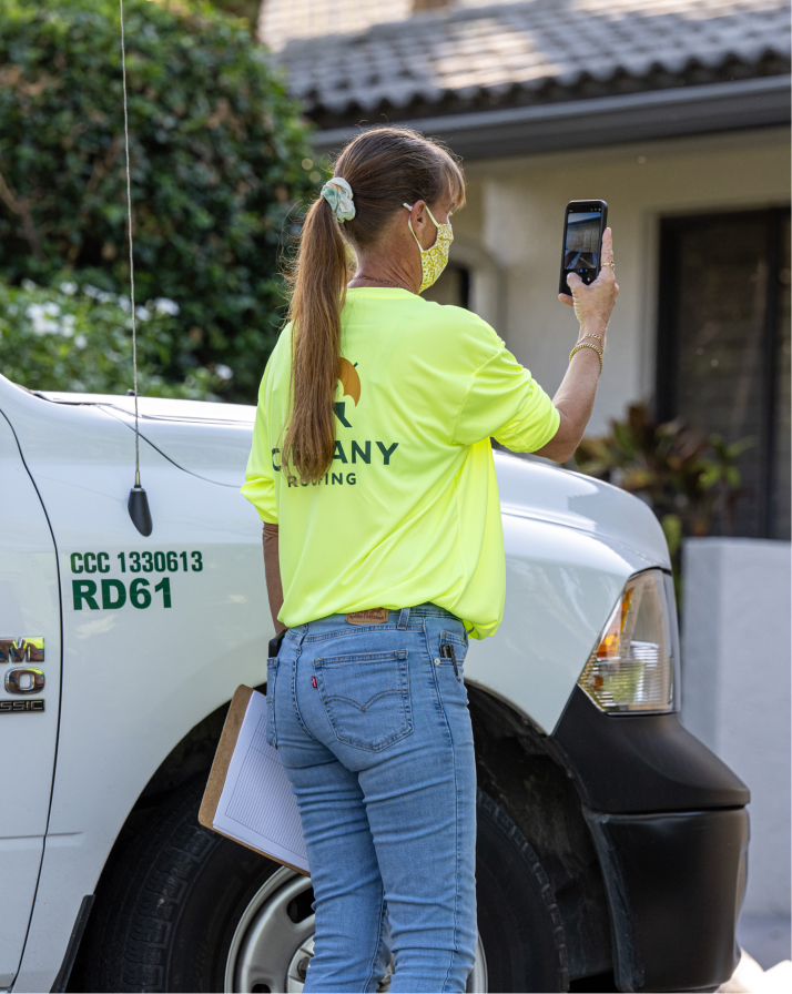 Campany technician in branded hi-vis photographing a roof condition beside a lettered company truck