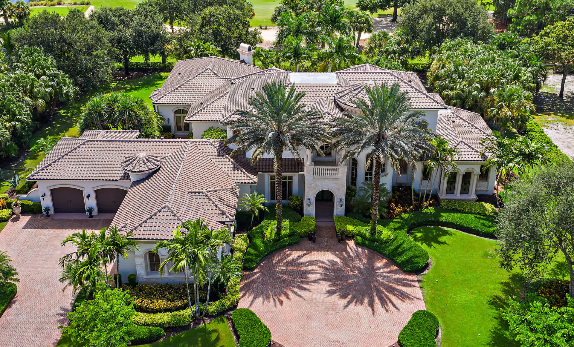 Aerial of a grand tile-roof estate with circular paver drive and palms