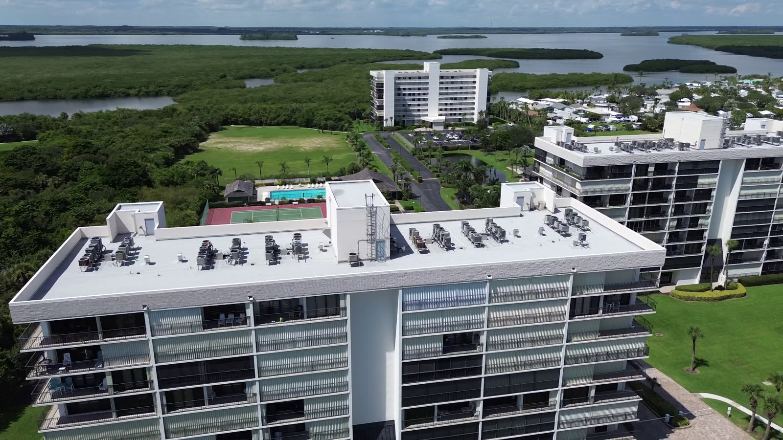 Drone still of several finished condominium towers over preserve and water